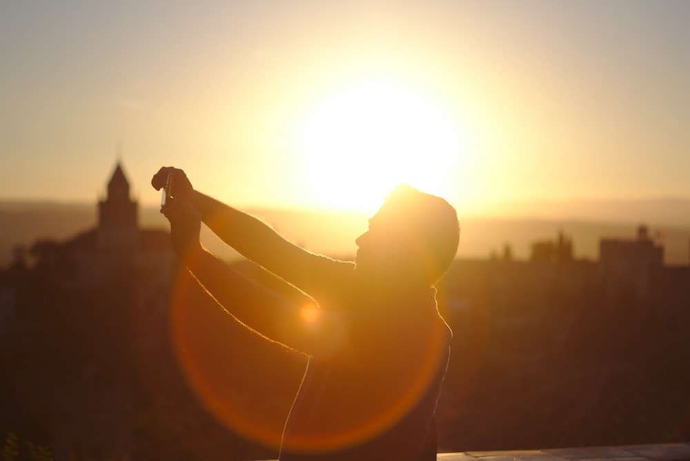 man holds up phone to take a selfie at sunset