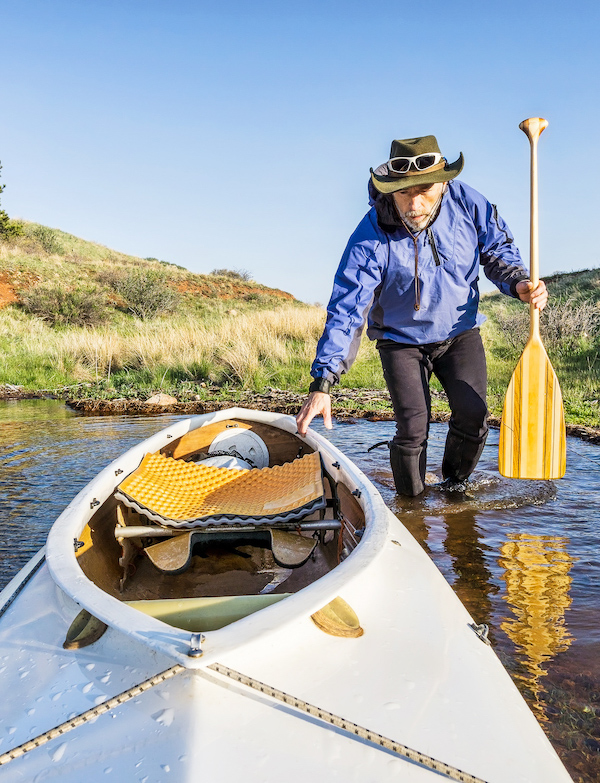 man loads a kayak into a body of water