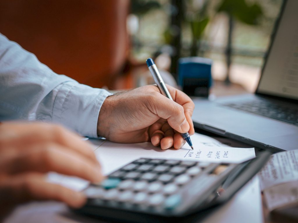 close up of a person using a calculator to do math and write down figures