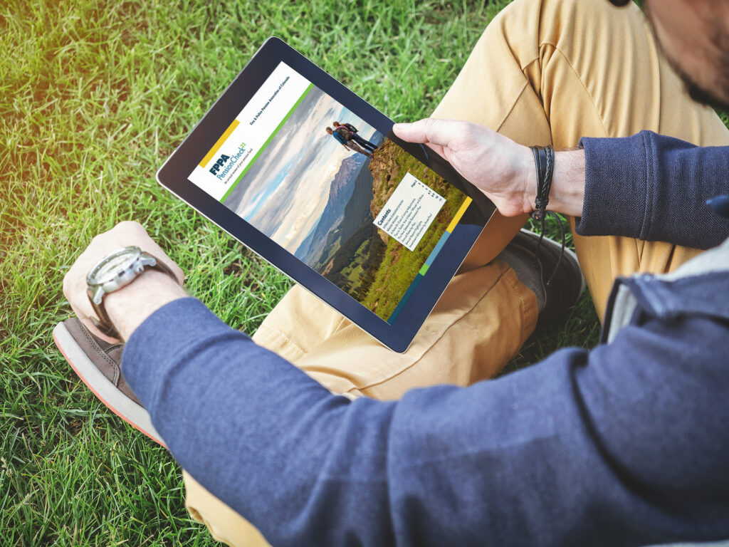 A man sits in a field, reading a copy of FPPA's newsletter on a tablet