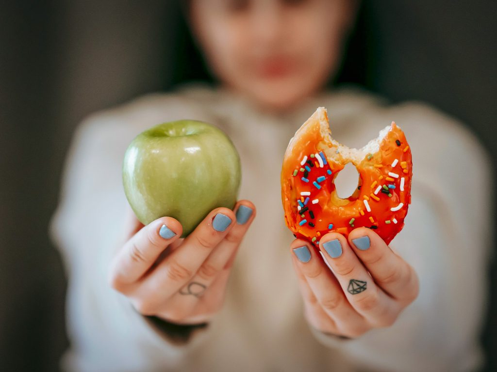 A person holds up an apple and a doughnut for comparison