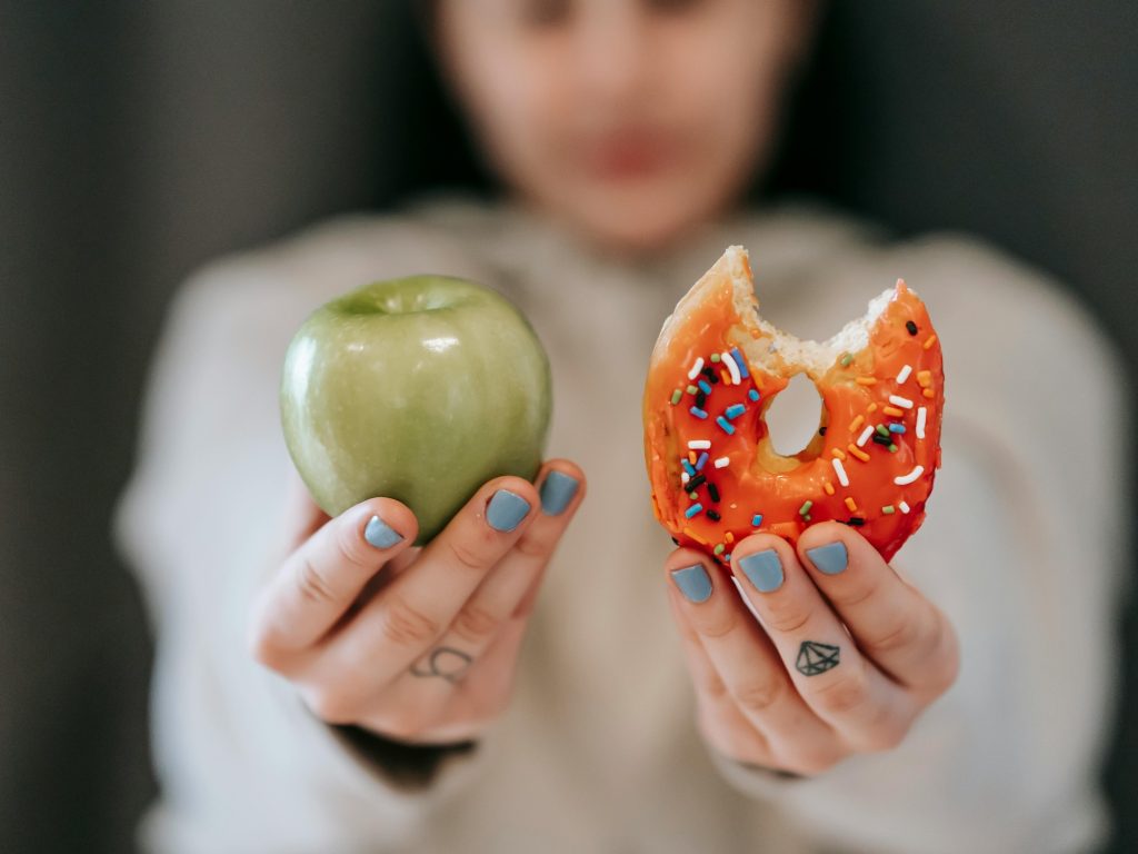 A person holding up an apple and a doughnut for comparison