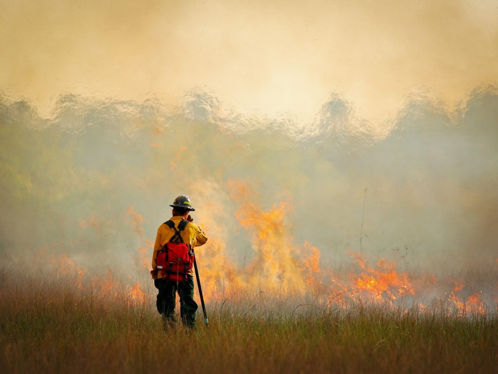 Grassland firefighter stands in front of a small grass fire