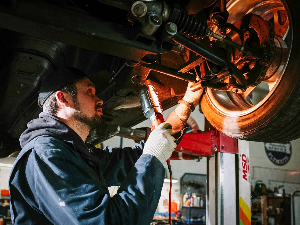 A mechanic holds a light to inspect the back side of a car's wheel